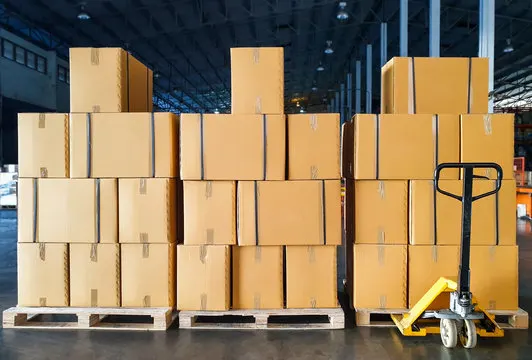 Cajas apiladas sobre pallets con zorra hidráulica en depósito